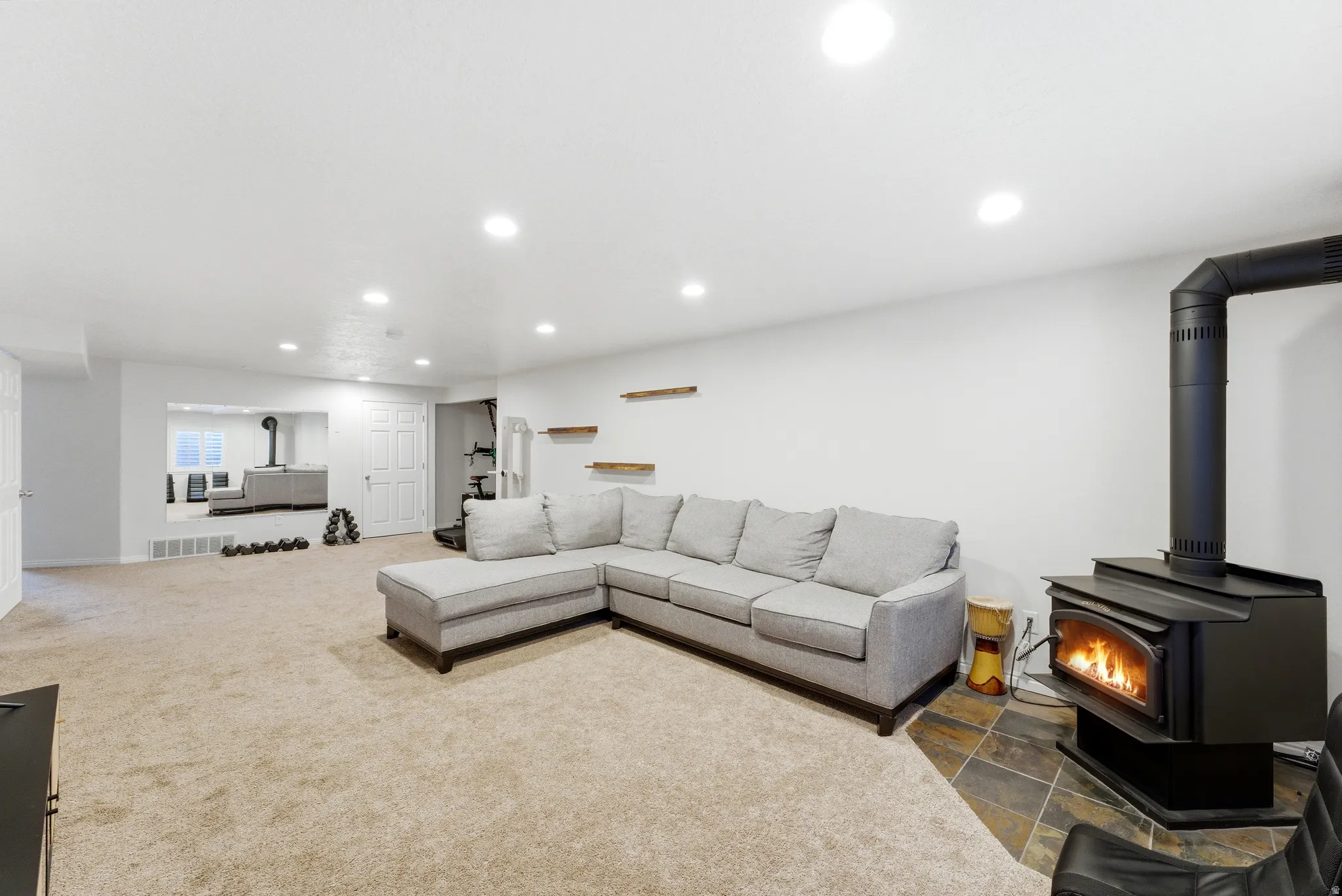 Spacious room with a wood-burning stove on a slate tile hearth, recessed lighting, and light-toned carpet flooring