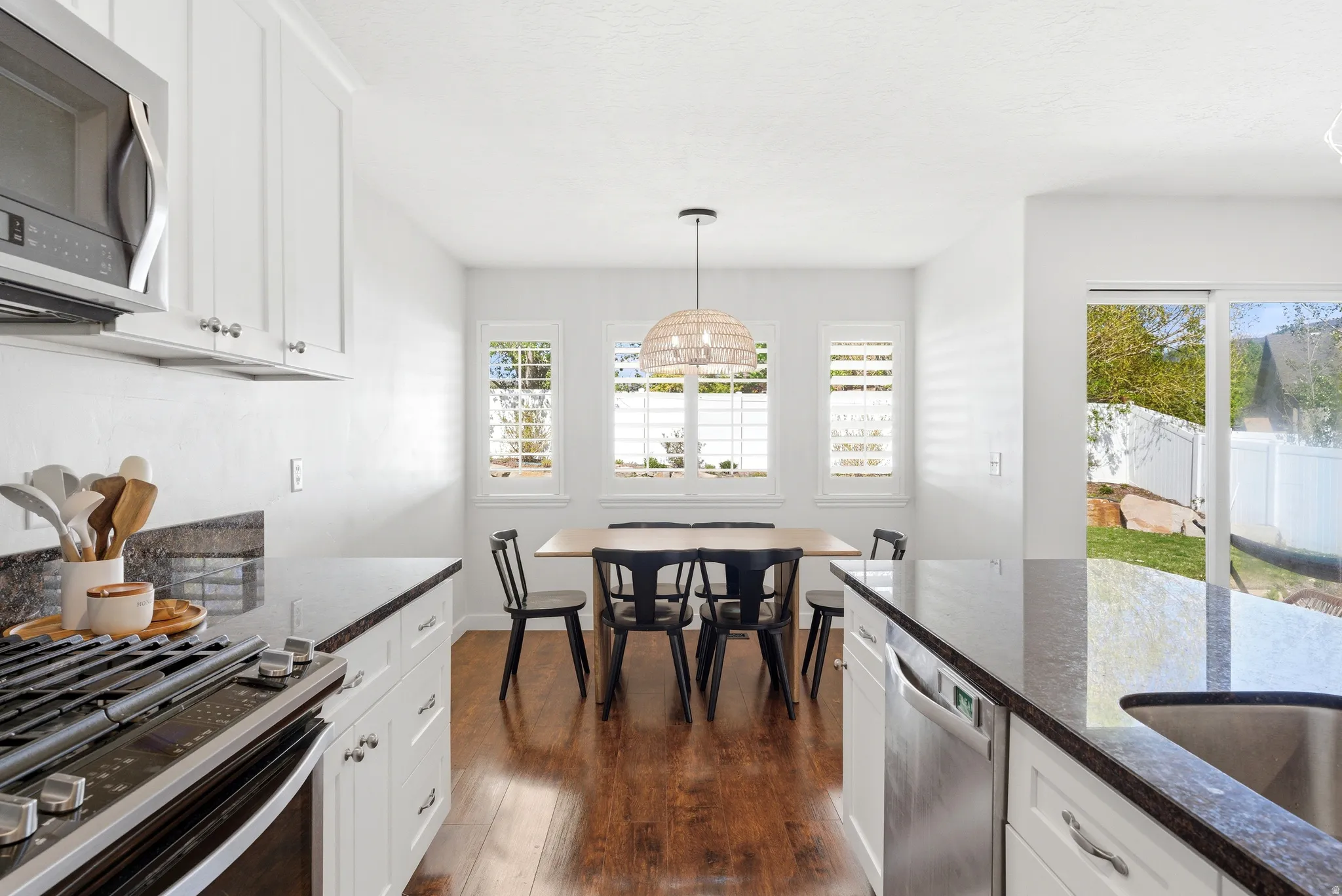 Kitchen featuring white cabinetry, dark stone countertops, stainless steel appliances, and wood-finish flooring