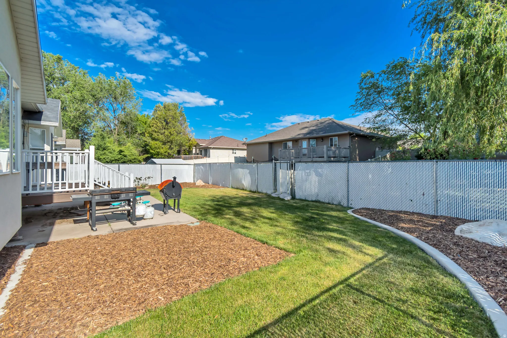 Expansive backyard featuring a manicured lawn, a large concrete patio, and a dedicated wood chip area