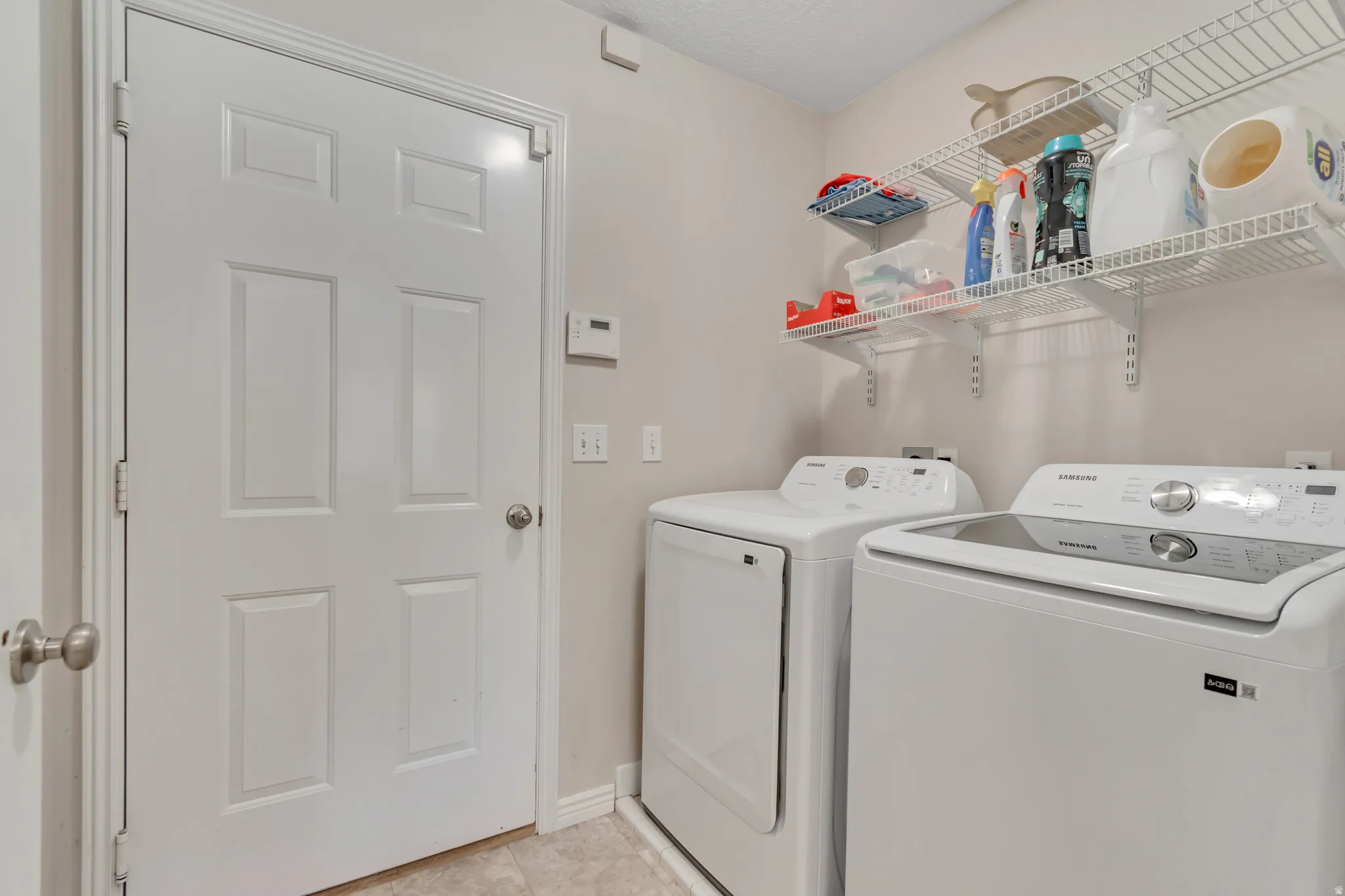 Dedicated laundry area featuring a white six-panel door, vinyl flooring, two built-in wire shelving units, and light neutral wall paint