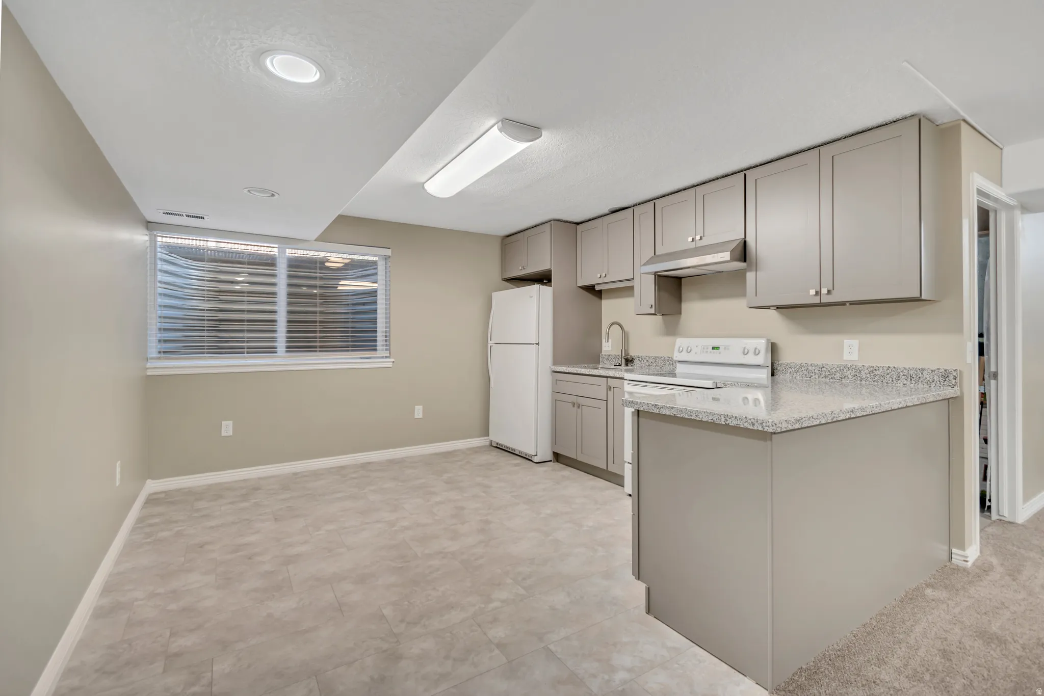 Kitchen space featuring light gray cabinetry, speckled countertops, and tile-finish flooring