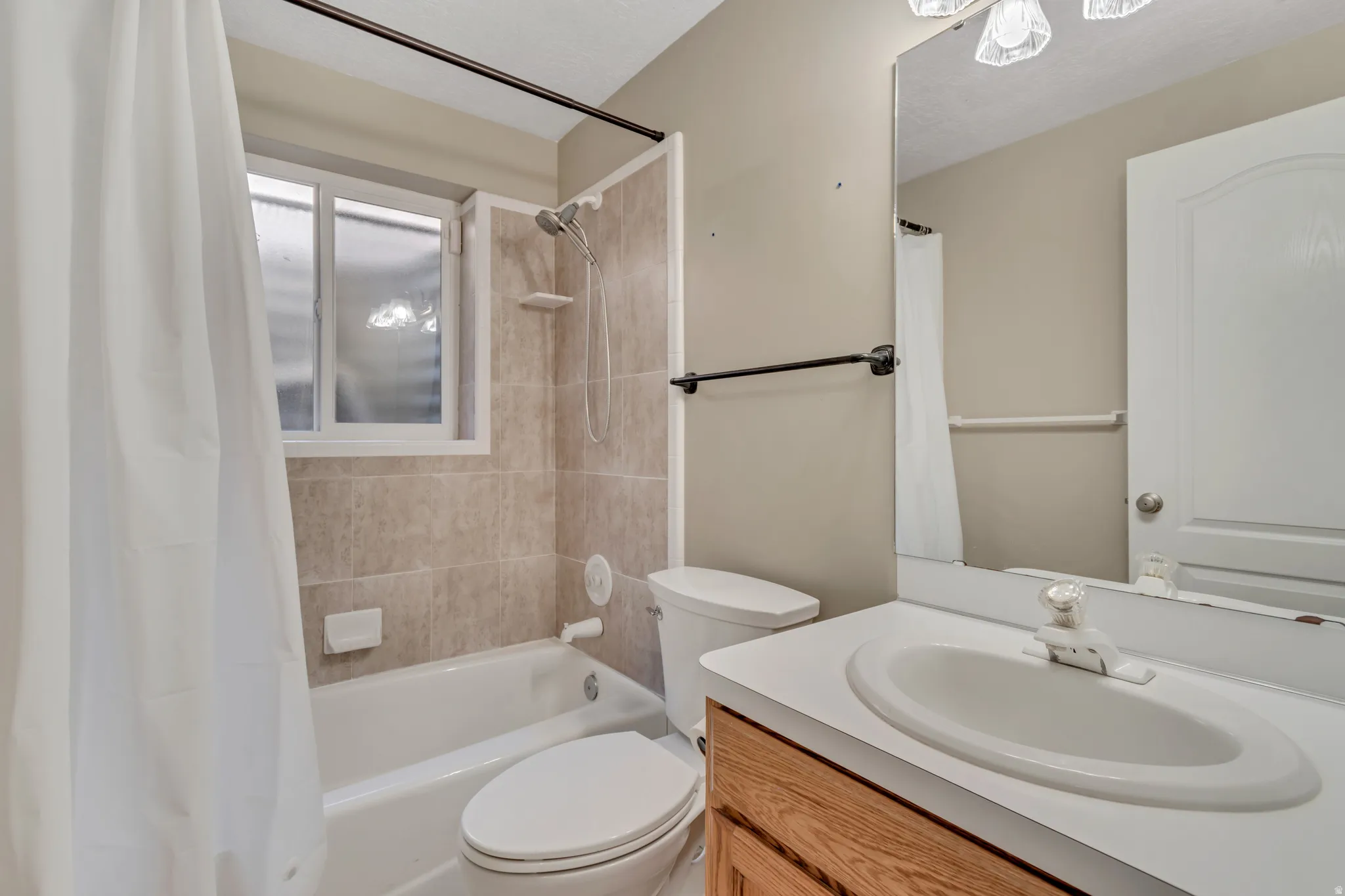Bathroom featuring a white tub, tiled shower surround, frosted window, and a vanity with an integrated sink and wood-finish cabinetry