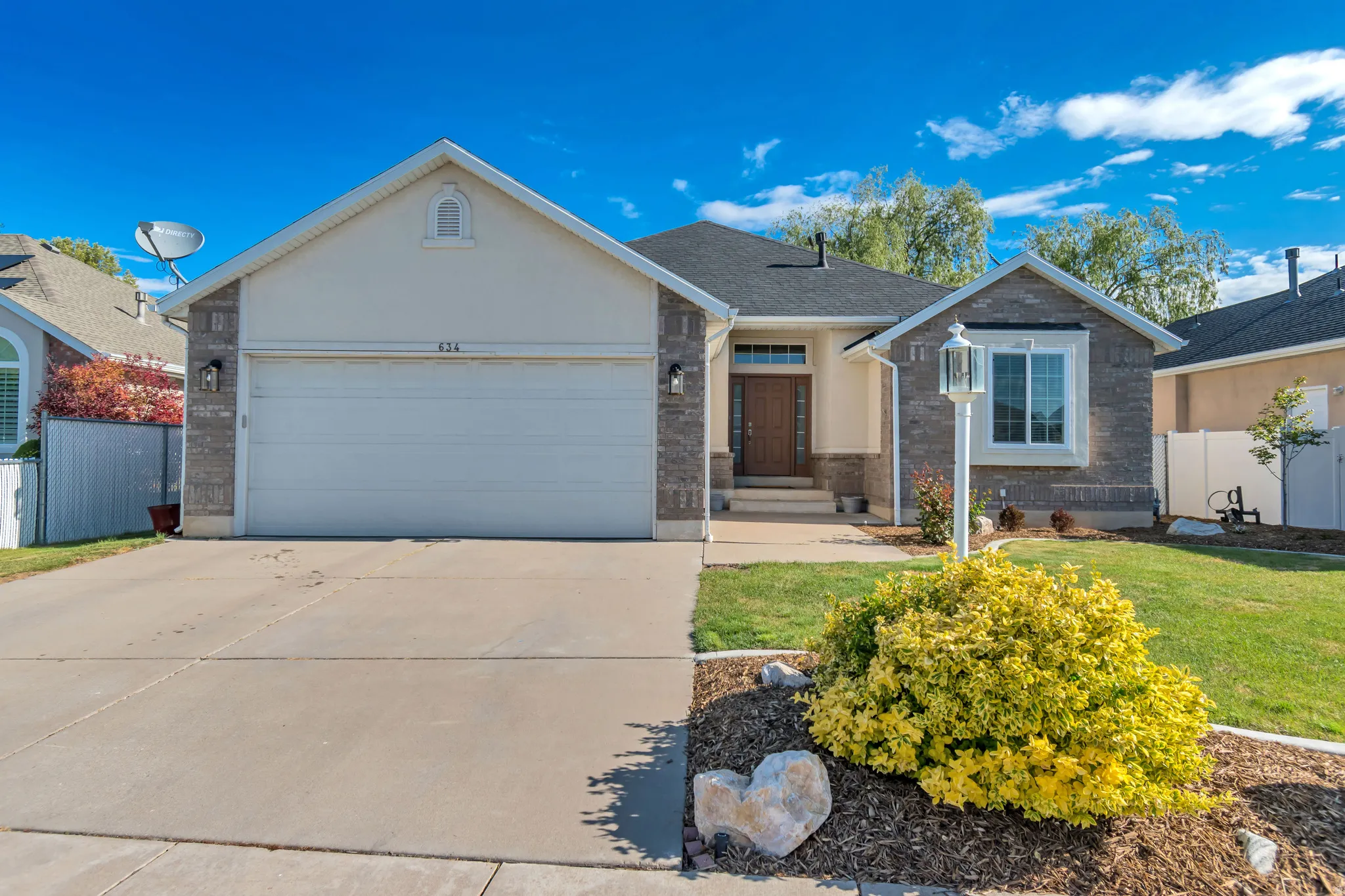 Exterior featuring a two-car garage, stone facade accents, a wood-finish entry door, a paved driveway, and a landscaped front yard with a decorative lamppost