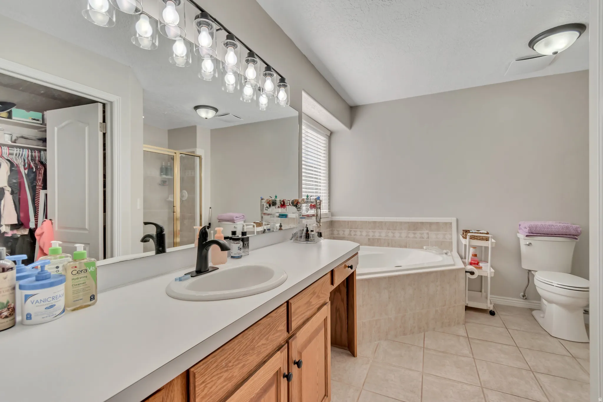 Bathroom with wood-finish cabinetry, a large vanity mirror, and a built-in tub with tile surround