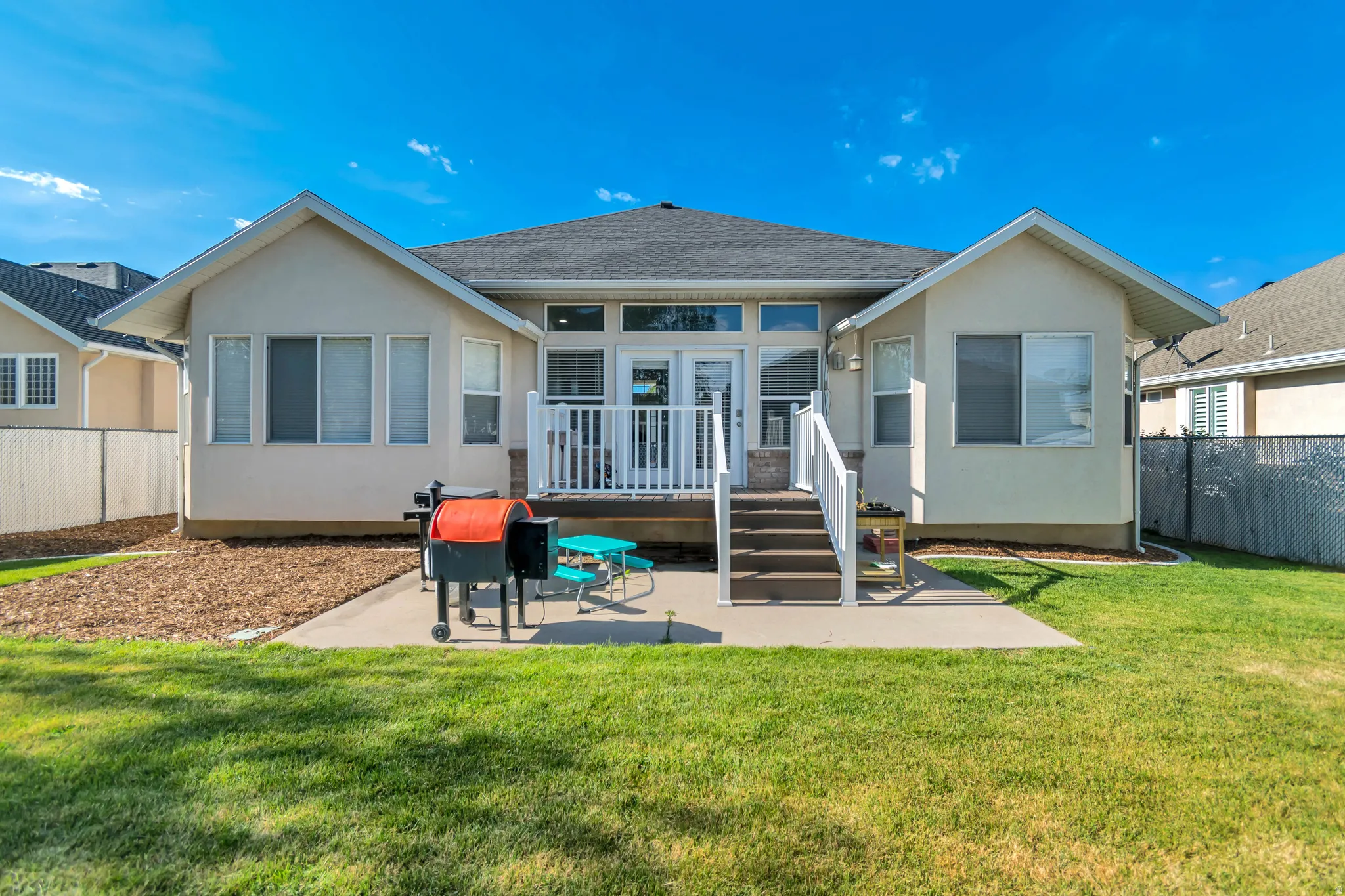 Expansive backyard featuring a manicured lawn, a large concrete patio, and a wood-finish deck with white railings