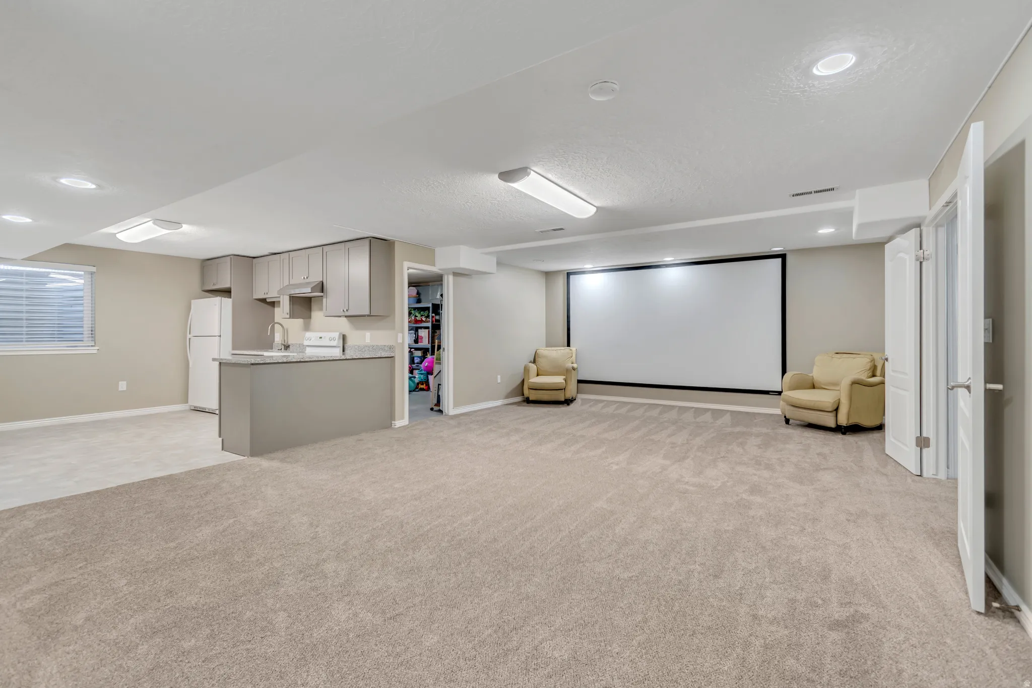 Spacious lower-level living area featuring a built-in projection screen, recessed lighting, and soft carpet flooring