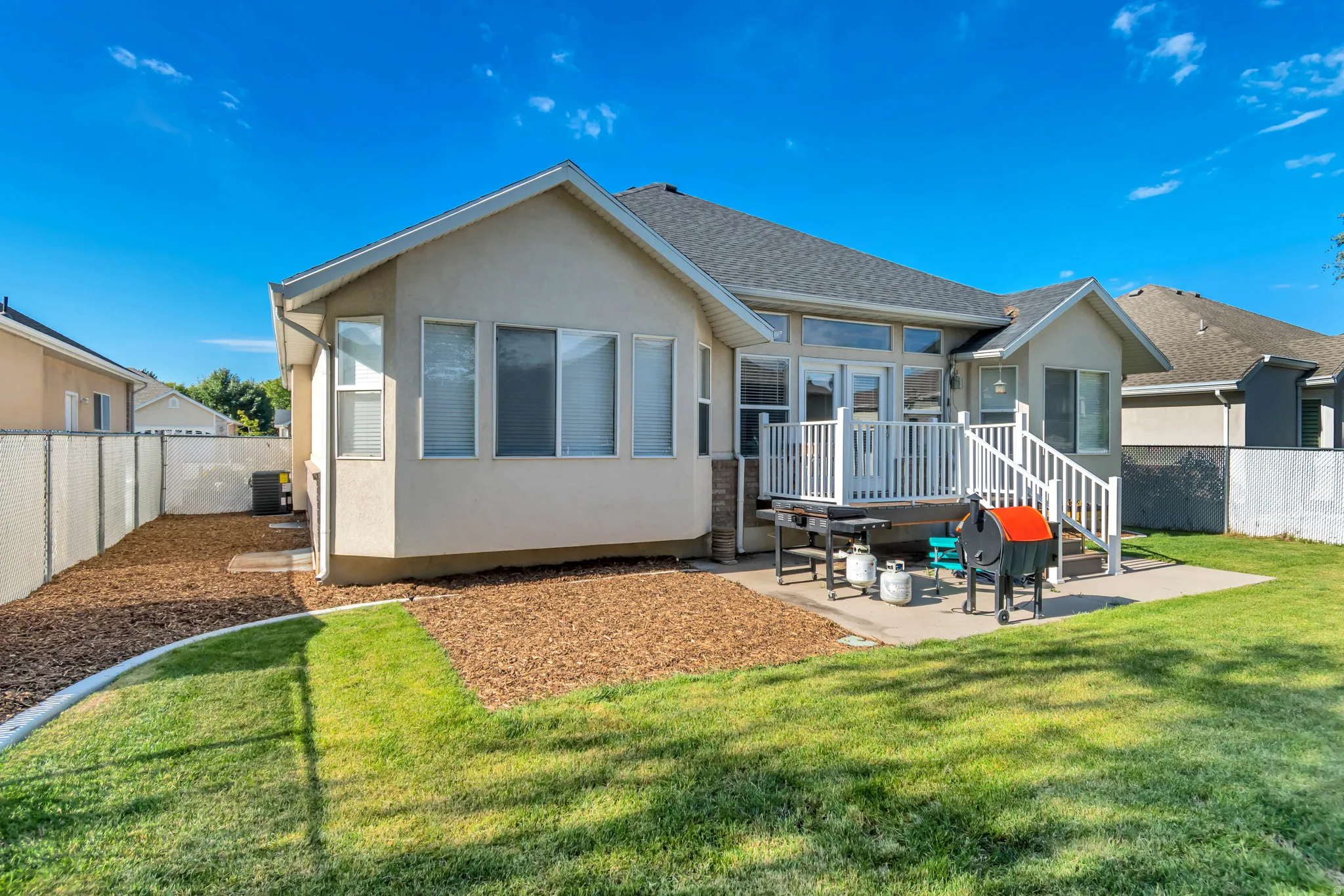 Rear exterior featuring a spacious elevated deck with white railing, a concrete patio, and a manicured lawn