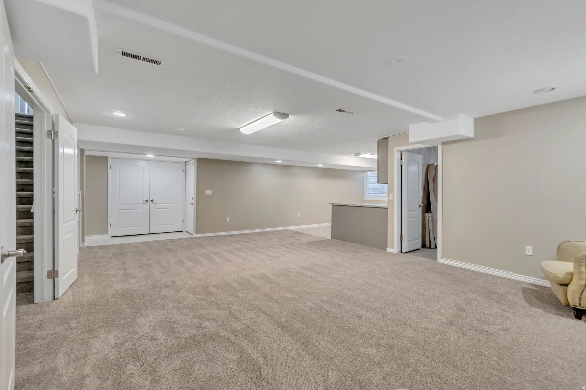 Expansive carpeted room featuring recessed lighting, a built-in breakfast bar with a solid surface countertop, and double paneled doors
