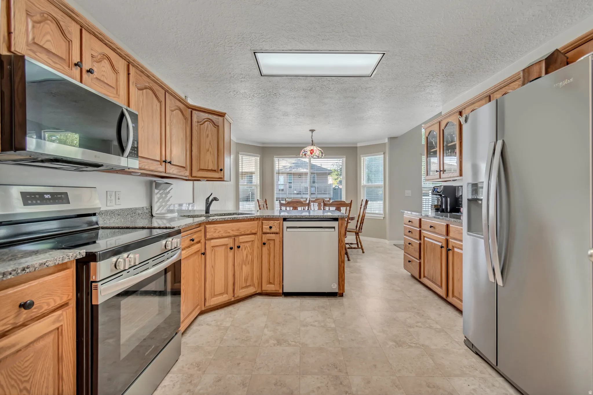 Spacious kitchen featuring wood cabinetry, stainless steel appliances, dark countertops, a built-in dishwasher, and light tile flooring