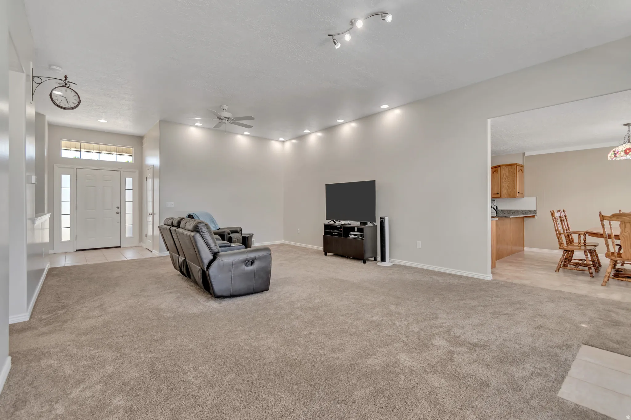 Spacious living area featuring neutral carpeting, recessed ceiling lighting, a ceiling fan, and a wide entryway with transom window and sidelights