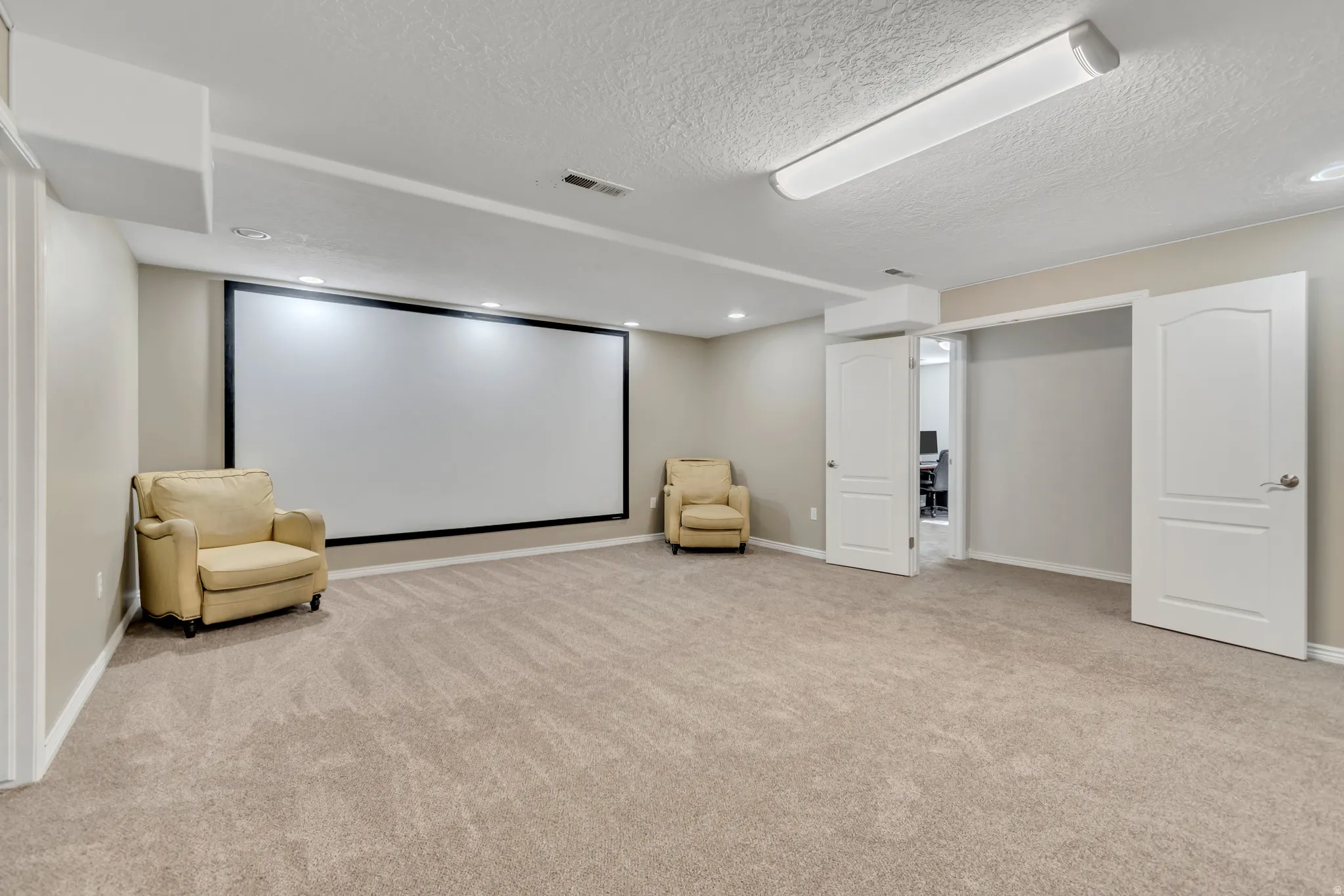 Spacious media room featuring a large projection screen, recessed lighting, and neutral-toned carpeting