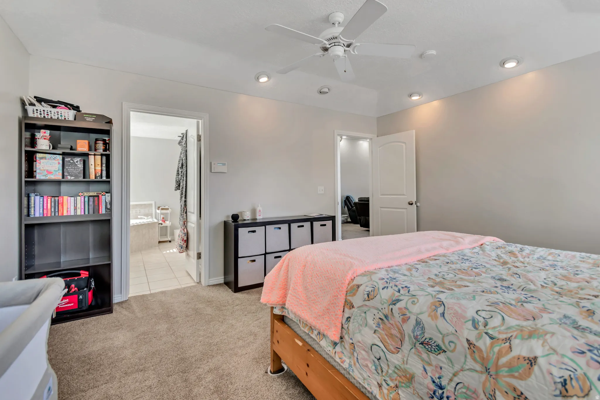 Carpeted bedroom featuring a tray ceiling with a ceiling fan, recessed lighting, and a white interior door leading to a tiled bathroom with a built-in tub