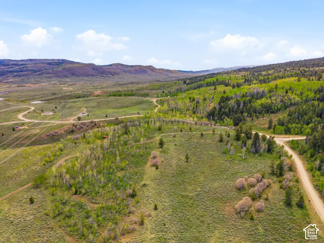 Expansive terrain featuring varied topography, natural vegetation, unpaved roads, and distant structures