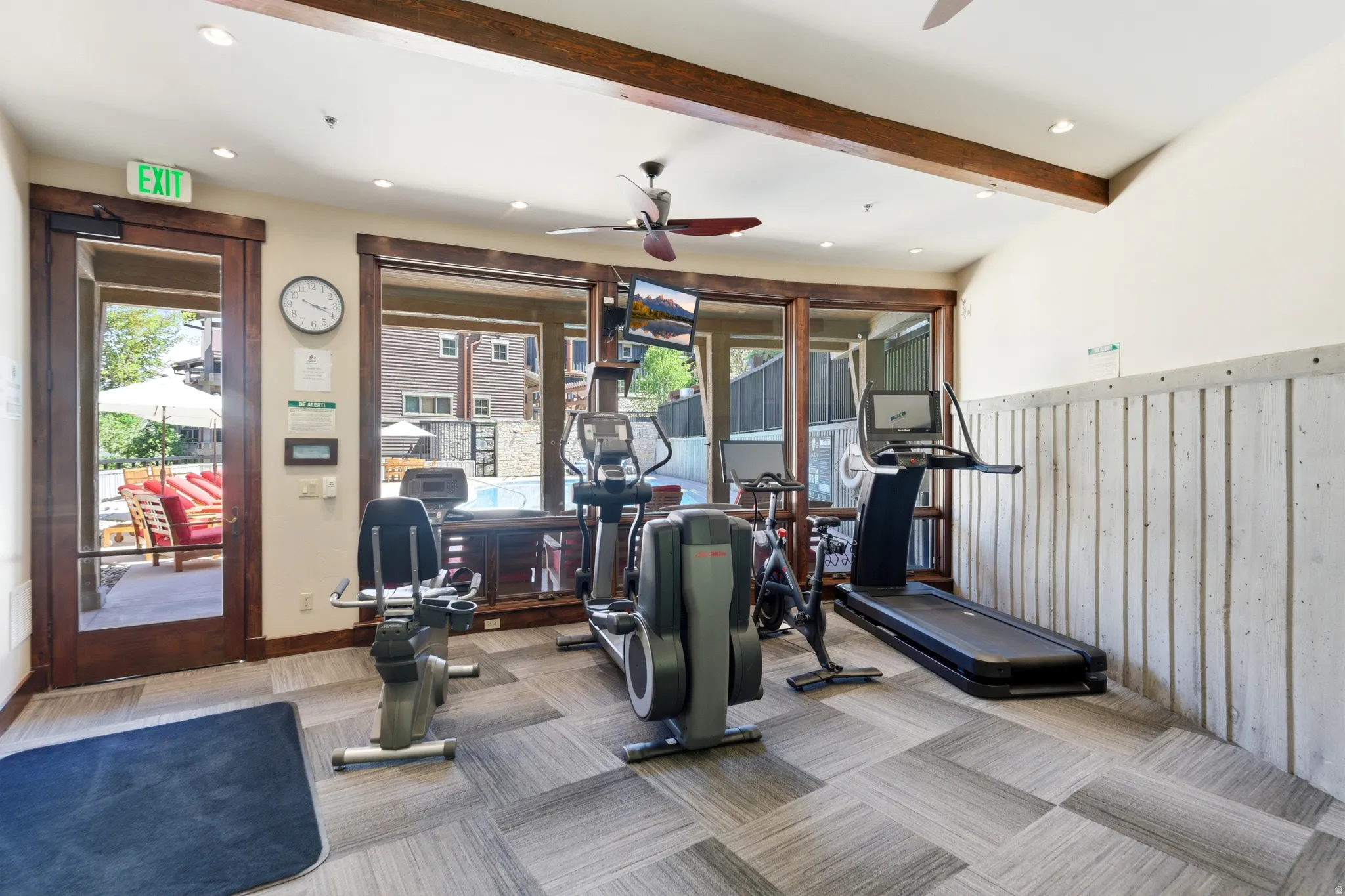 Fitness center featuring wood-finish ceiling beams, recessed lighting, and a large window overlooking a swimming pool