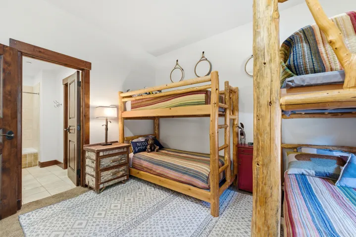 Bedroom featuring two wood-frame bunk beds, a patterned area rug, and a wood-paneled door opening to a bathroom with tiled flooring and a shower