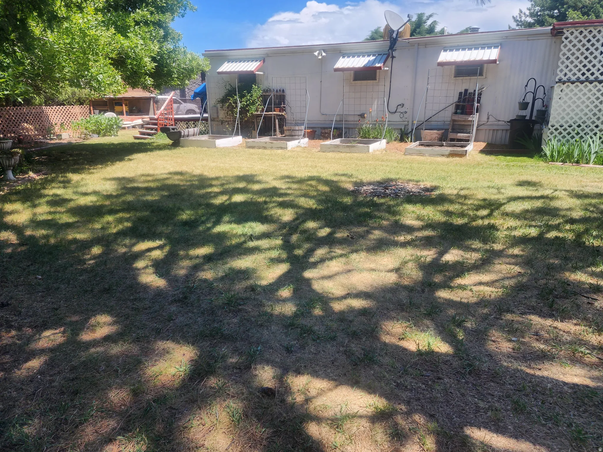 Expansive backyard featuring a large grass area, raised garden beds, and a white lattice fence