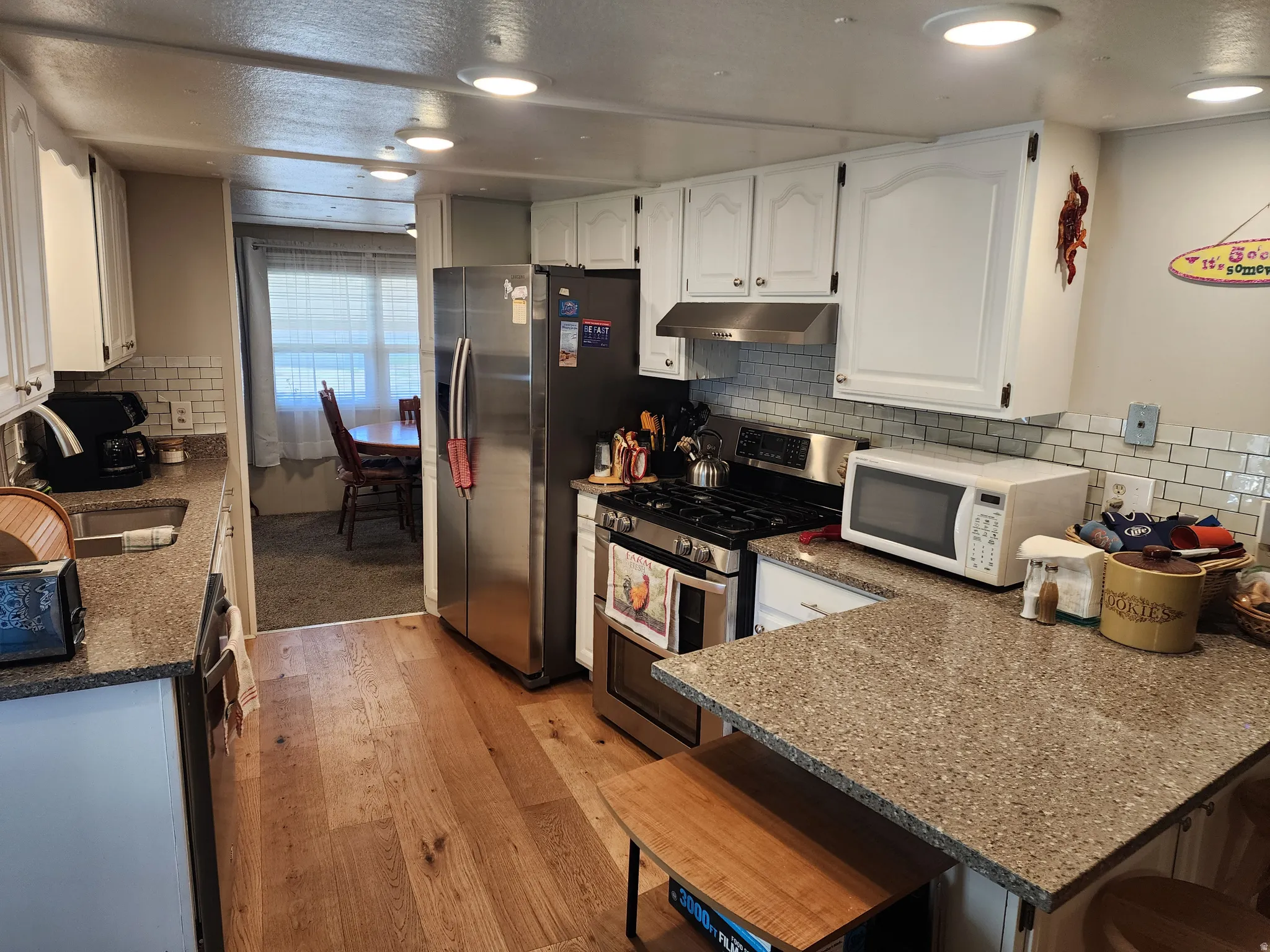Kitchen featuring wood-finish flooring, white cabinetry, a subway tile backsplash, and speckled countertops