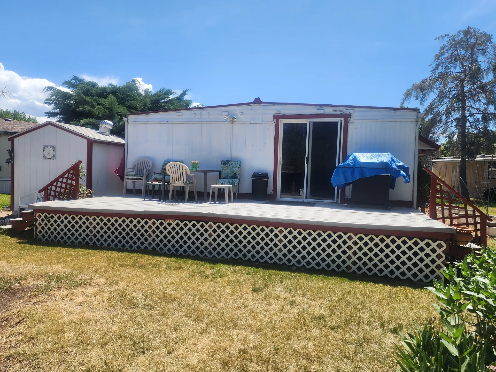 Rear exterior featuring a spacious deck with lattice skirting, sliding glass door, and a detached shed