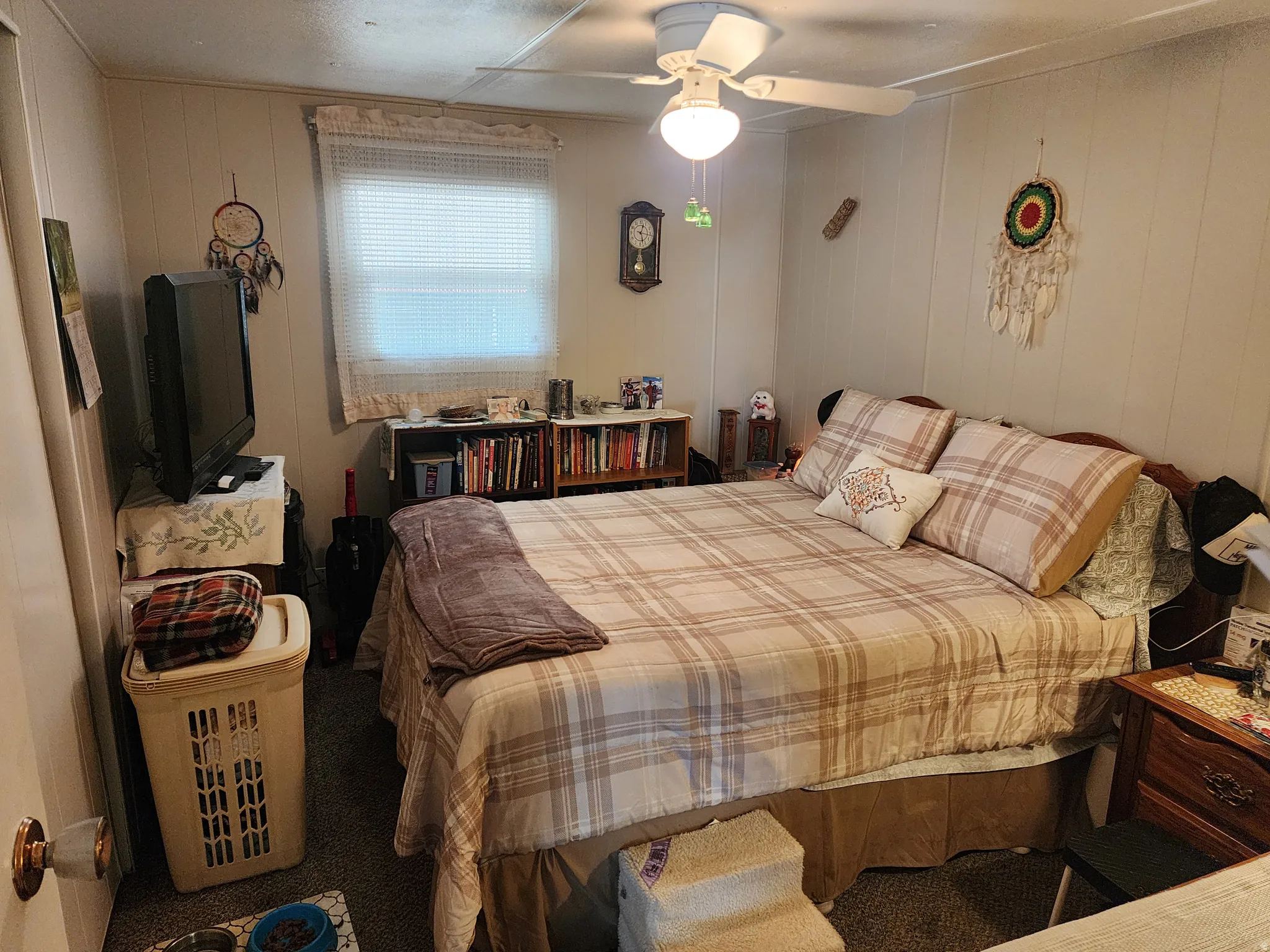 Carpeted interior room featuring vertical paneling, a ceiling fan with integrated lighting, a window with horizontal blinds, and a built-in bookshelf