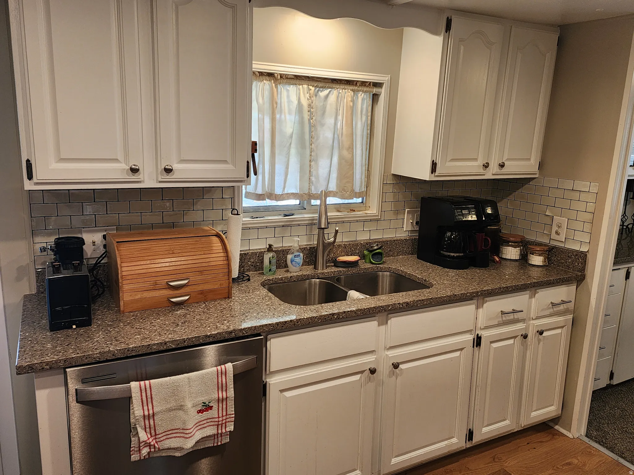 Kitchen featuring white shaker-style cabinetry, a stainless steel double basin sink with a gooseneck faucet, a light-colored subway tile backsplash, and speckled countertops