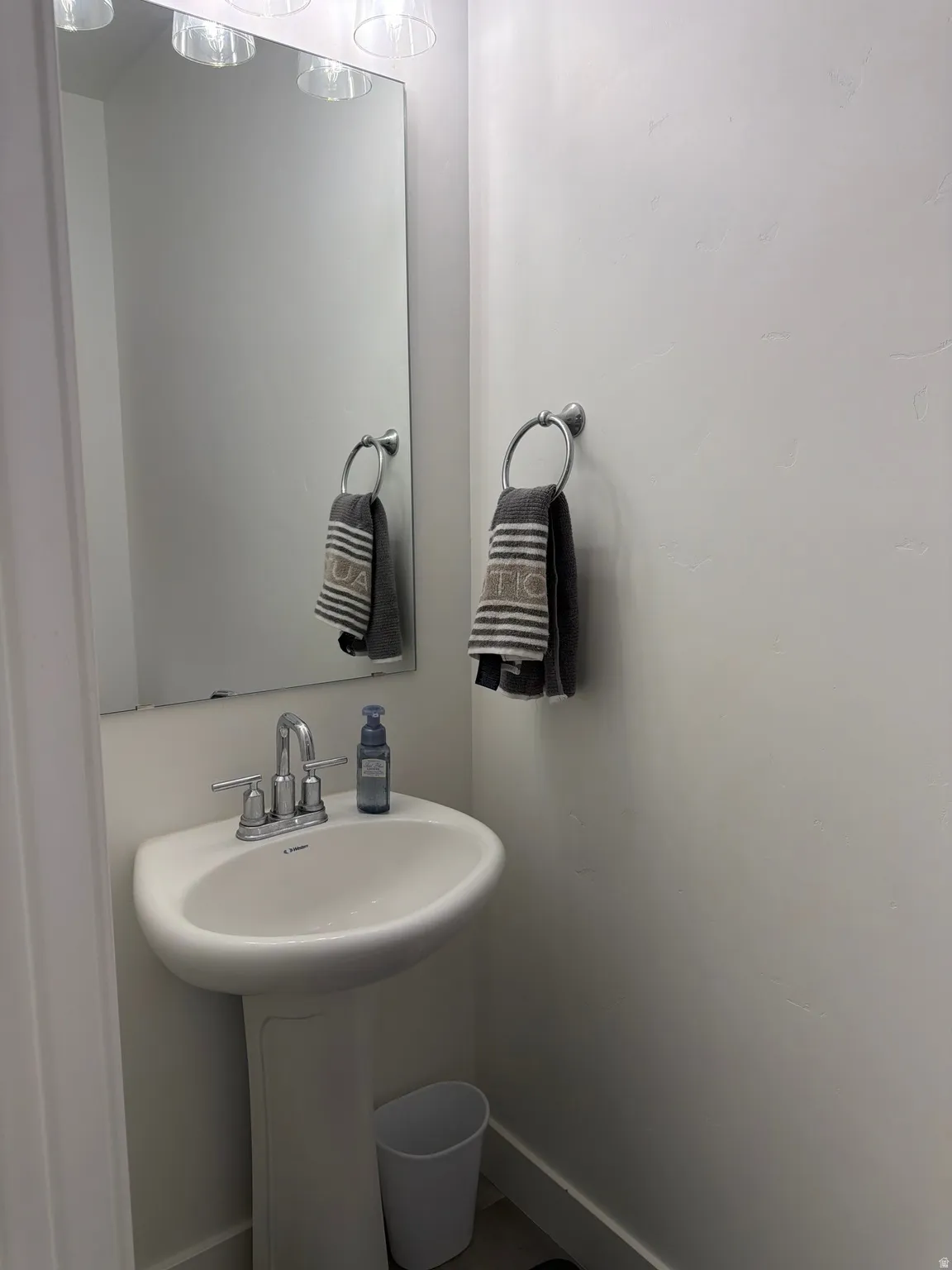 Pedestal sink with chrome faucet, large frameless mirror, and overhead vanity lighting