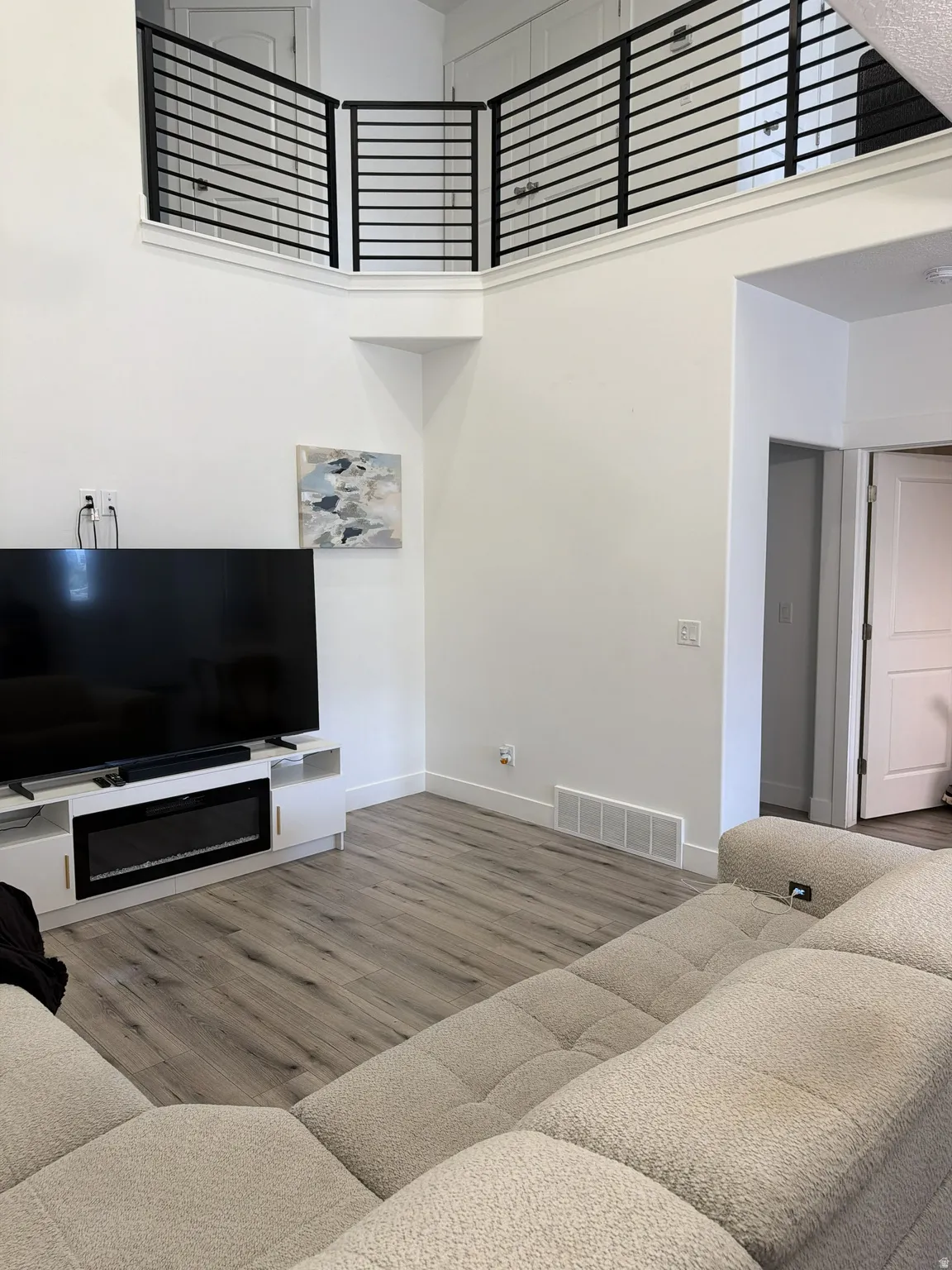 Two-story living area featuring a built-in entertainment console with an electric fireplace, wood-finish flooring, and a second-story balcony with modern black railings