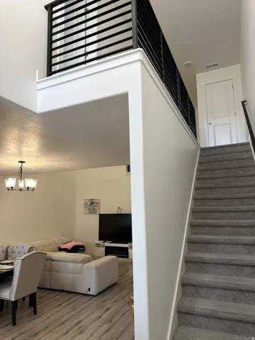 Split-level interior featuring a carpeted staircase with a dark handrail, a second-story landing with black horizontal slat railing, and a vaulted ceiling