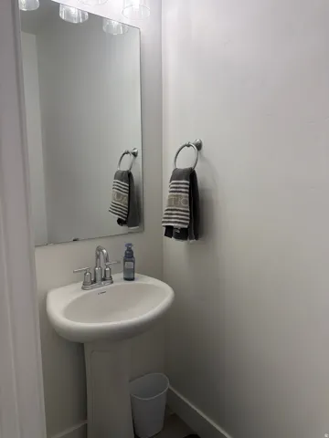 Pedestal sink with chrome faucet, large frameless mirror, and overhead vanity lighting