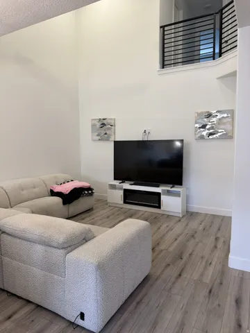 Vaulted living area featuring wood-finish flooring, a contemporary media console with an electric fireplace, and a second-story balcony with modern black railings