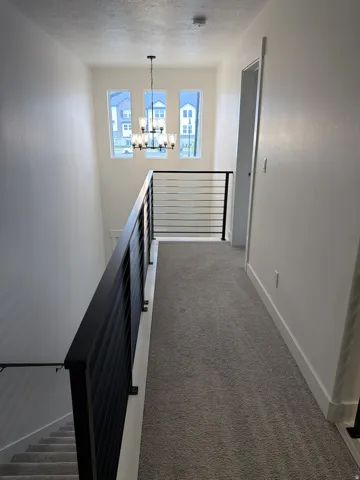 Upper-level hallway featuring a contemporary chandelier, three vertical windows, and a modern horizontal bar railing system