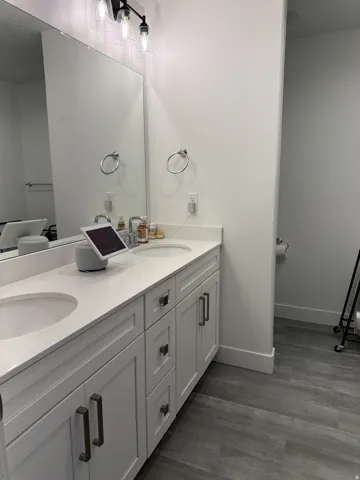 Dual vanity with integrated sinks, white cabinetry, and gray wood-finish flooring