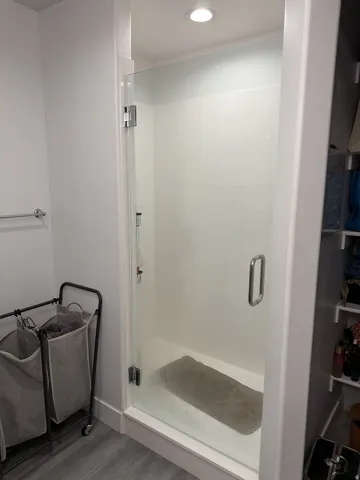 Glass-enclosed shower with a bright white surround and recessed ceiling lighting