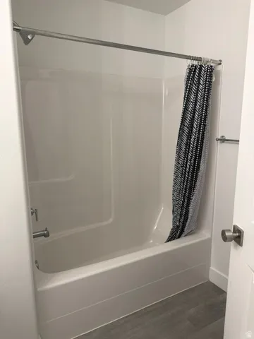 Tub and shower combination featuring a white surround, chrome fixtures, and a coordinating shower rod