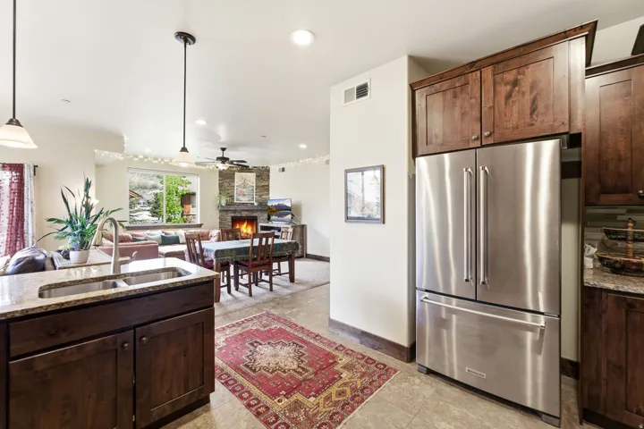 Kitchen with wood-finish cabinetry, stainless steel French door refrigerator, and a granite countertop island with an undermount double basin sink