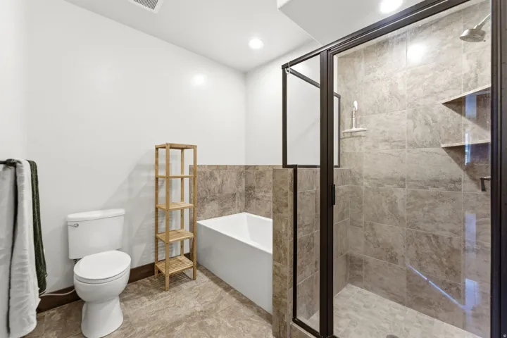 Bathroom featuring a glass-enclosed shower with tile surround and built-in shelving, a deep soaking tub, and a white toilet