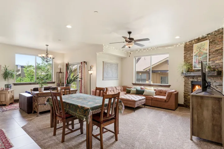 Open-concept living space featuring a stacked stone fireplace with wood mantel, a ceiling fan, large windows, and a sliding glass door