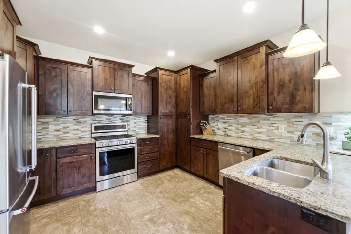 Spacious kitchen featuring dark wood cabinetry, stainless steel appliances, granite countertops, a tiled backsplash, and recessed lighting