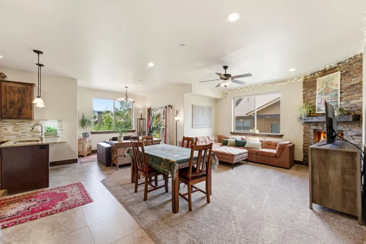 Open-concept living area featuring a stacked stone fireplace, large windows, recessed lighting, and a ceiling fan