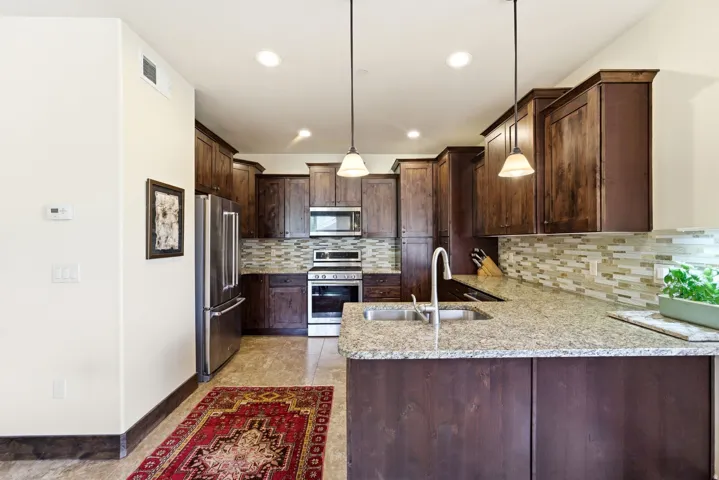Kitchen featuring wood cabinetry, stainless steel appliances, speckled countertops, and a tiled backsplash