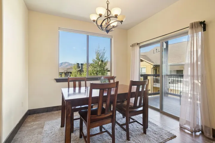 Dining area featuring a large window, sliding glass door with balcony access, tiled flooring, baseboard trim, and a decorative chandelier