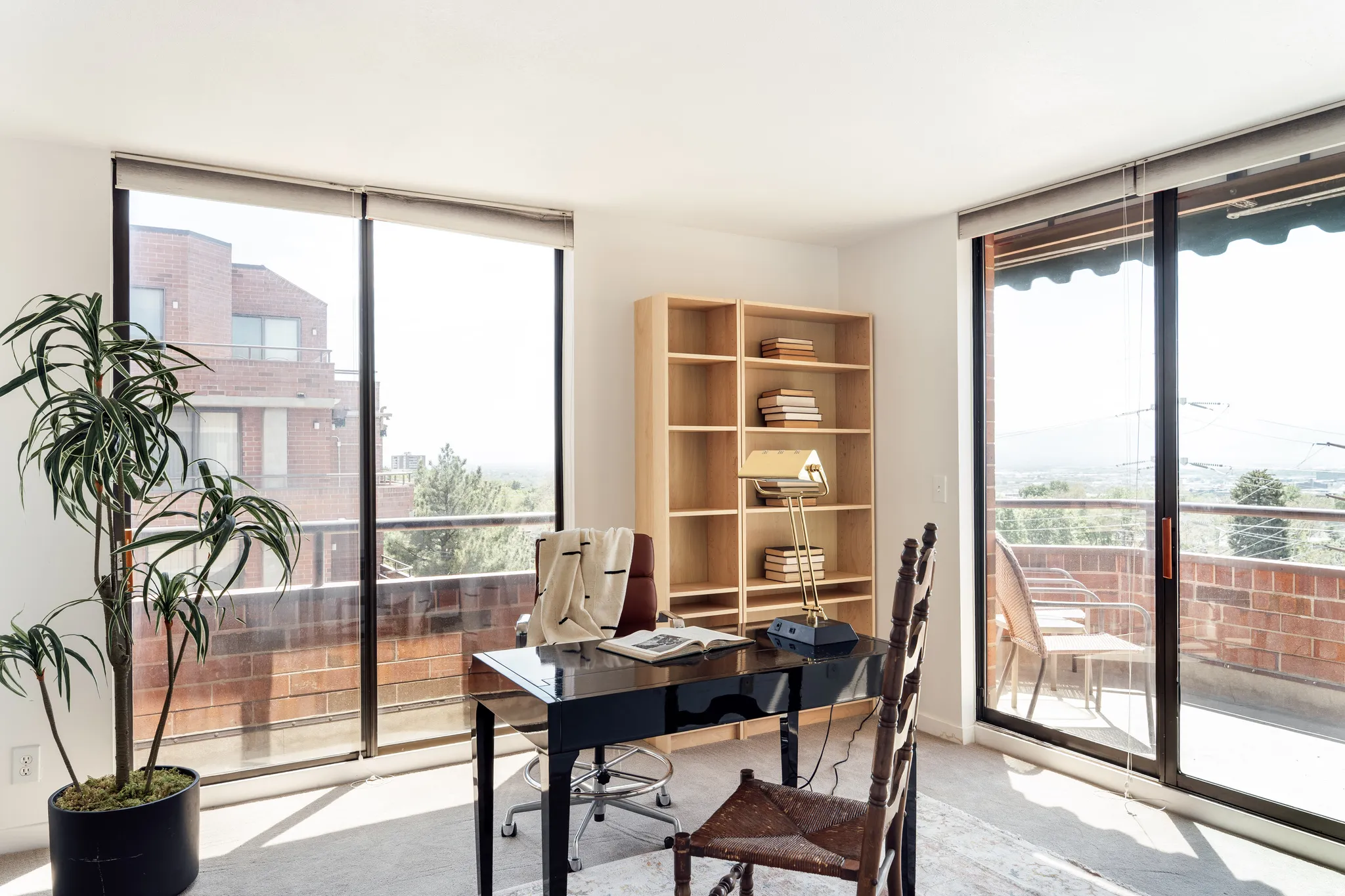 Bright room featuring extensive natural light, full-height windows, a built-in wooden bookshelf, and direct access to an exterior balcony