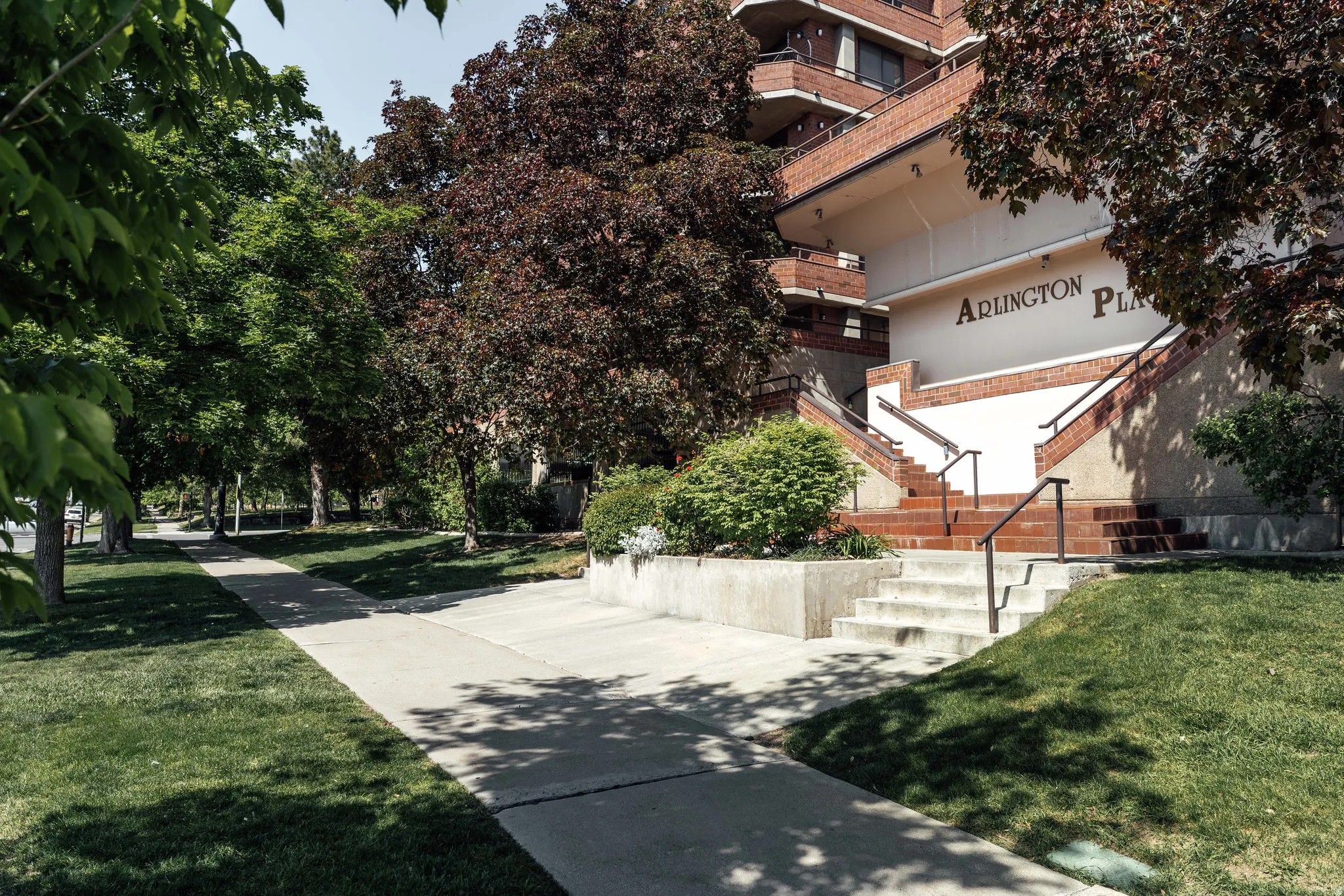 Arlington Place building entrance featuring brick and concrete stairs, black metal railings, and integrated landscaping