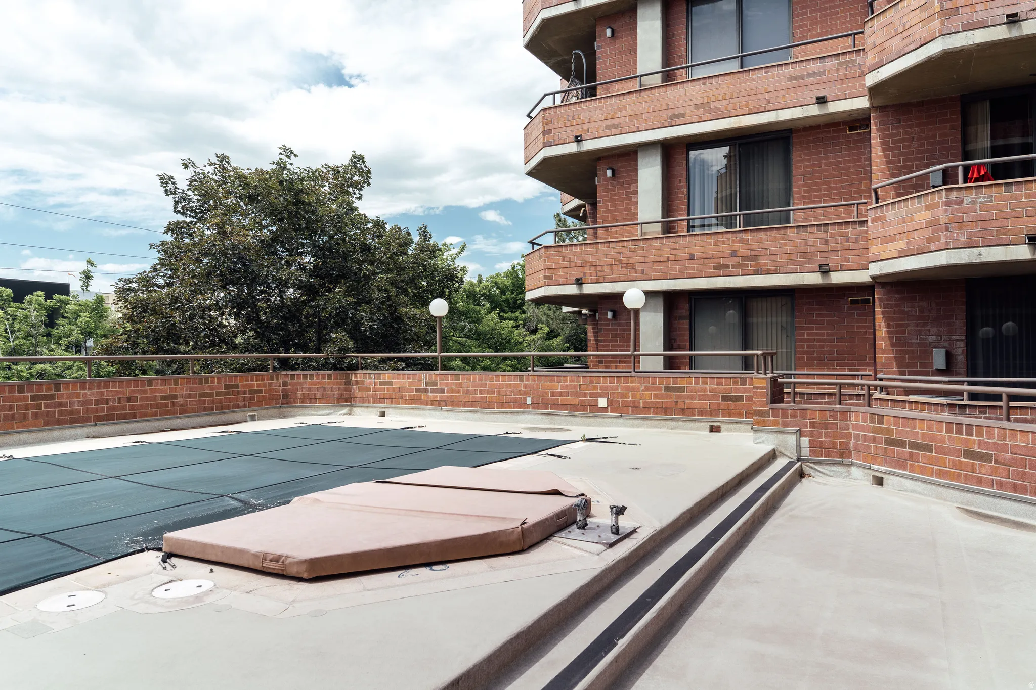 Rooftop amenity space featuring a covered swimming pool, a covered hot tub, and surrounding brick walls with metal railings