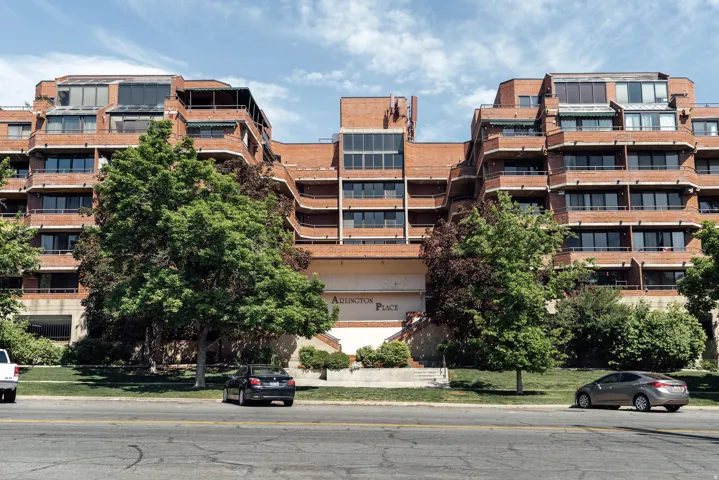 Brick facade building with multiple levels of balconies, individual window awnings, and mature landscaping