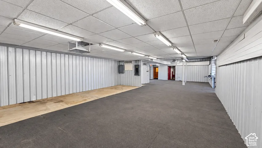Expansive interior space featuring corrugated metal walls, a drop ceiling, fluorescent lighting, and carpeting