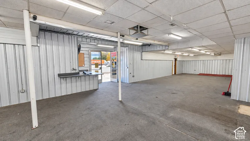 Spacious interior featuring corrugated metal wall panels, exposed structural beams, and suspended acoustic ceiling tiles with fluorescent lighting