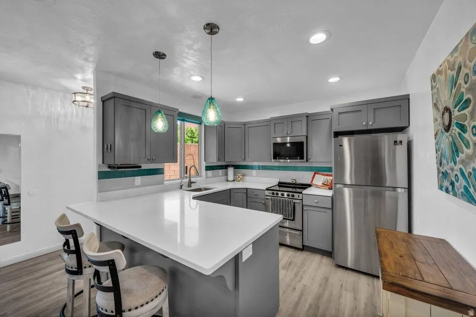 Kitchen featuring grey cabinetry, stainless steel appliances, a white countertop island, pendant lighting, and wood-finish flooring