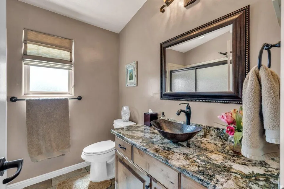 Bathroom featuring a wood-finish vanity with a vessel sink, a stone countertop, and a framed mirror