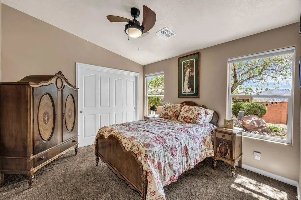 Carpeted room with a vaulted ceiling, a ceiling fan with integrated lighting, and two large windows