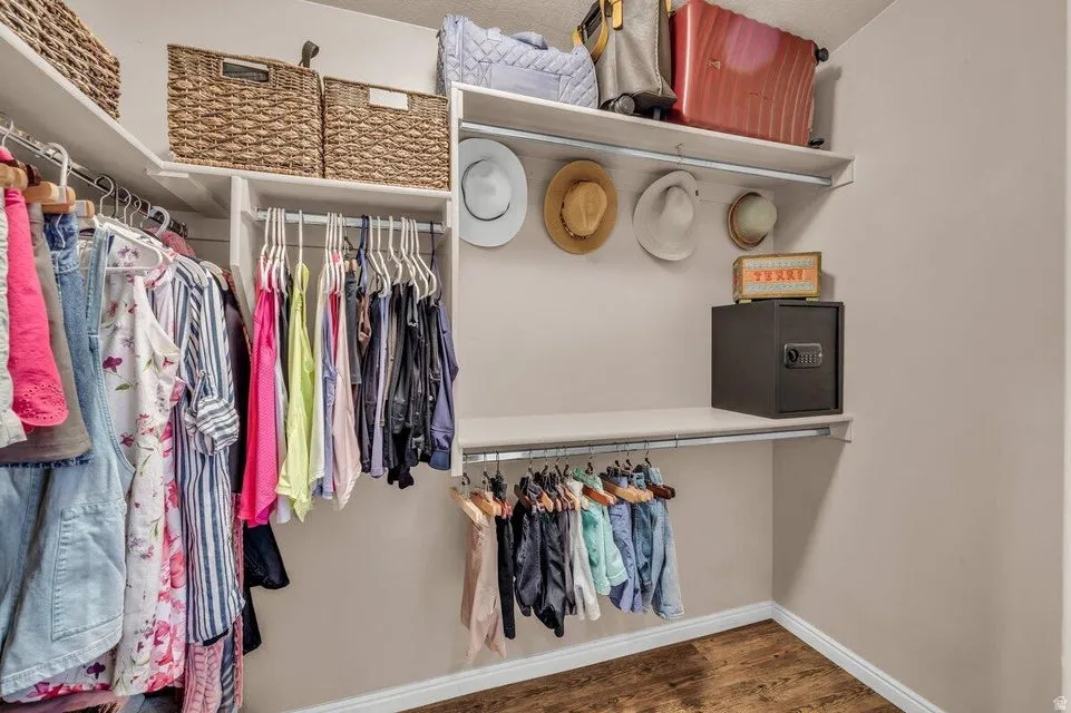 Walk-in closet featuring white shelving, multiple hanging rods, and wood-finish flooring